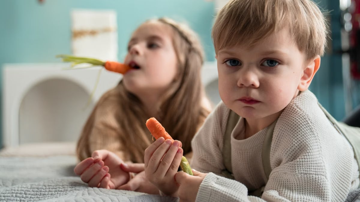 Siblings enjoy carrots together indoors, highlighting healthy eating and family time.